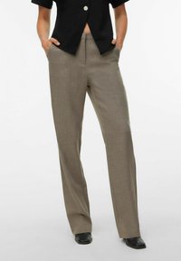 Pantalon kaki à coupe ajustée, devant plat et jambes droites, fabriqué dans un tissu texturé. Avec poches, associé à un haut noir.