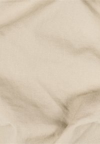 Béžová texturovaná tkanina s jemným tkaným vzorem a přirozenými záhyby vytvářejícími jemné stíny a odrazy světla.