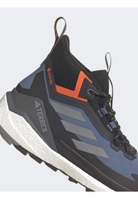 Wysokie buty sportowe w kolorystyce czarno-niebieskiej, z teksturowaną syntetyczną cholewką, pomarańczowymi akcentami i białą, grubą podeszwą.