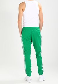 Zelené sportovní kalhoty s bílými bočními pruhy, elastickým pasem a bočními kapsami. Nosit se bílým tílkem a bílými teniskami.