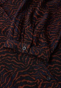 Chemise tissée en tissu noir avec un motif abstrait rouge et bleu. Dotée d'un détail de bouton et d'une texture plissée.