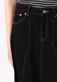 Svart denimskjørt med kontrasterende hvite sømmer, høy midje, frontlommer og avslappet passform. Detaljsømmen fremhever designet.