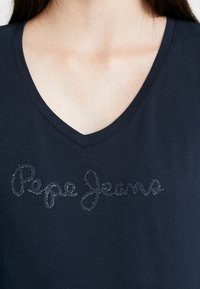 Mörkblå v-neck t-shirt med korta ärmar som har texten "Pepe Jeans" i en glansig, broderad kursiv design. Mjuk bomullstyg.
