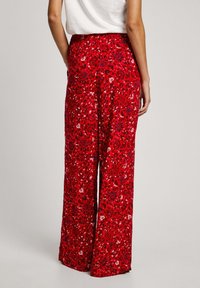 Pantaloni a gamba larga rossi a fiori presentano un motivo vivace con piccoli dettagli blu e bianchi, realizzati in tessuto leggero con una consistenza liscia.