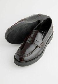 Mocassins en cuir verni bordeaux foncé avec un bout rond, des coutures décoratives et une semelle en caoutchouc noir texturée. Design sans lacets, facile à enfiler.