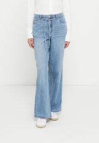 Ljusblå denimjeans med en avslappnad, vida ben, utrustade med skärp i midjan och framfickor. Kombinerade med vita sneakers.