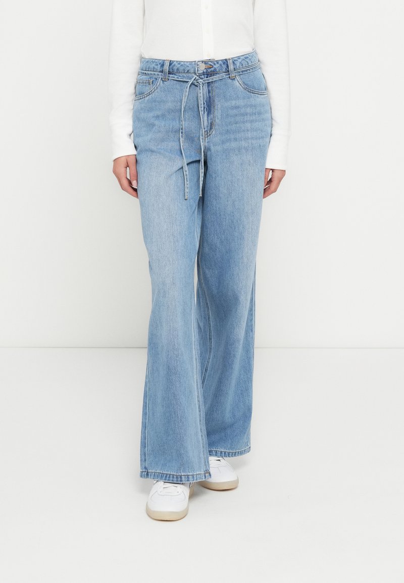 Ljusblå denimjeans med en avslappnad, vida ben, utrustade med skärp i midjan och framfickor. Kombinerade med vita sneakers.