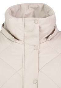 Veste matelassée beige clair avec un col haut rembourré et une fermeture par boutons-pression sur le devant.