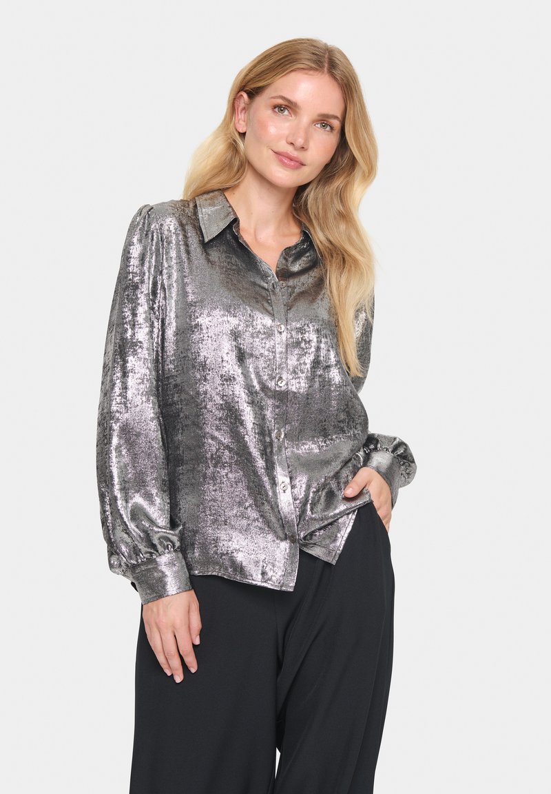 Silver metallic button-up shirt with a relaxed fit, featuring a spread collar, long puff sleeves, and smooth texture. Worn with loose black pants.