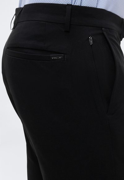 Μαύρο παντελόνι καμωμένο στα μέτρα με φερμουάρ στην πλαϊνή τσέπη και το λογότυπο RLX στην πίσω τσέπη, φορεμένο με ανοιχτό μπλε πουκάμισο με σχέδια, μπαρκάρισμένο μέσα.