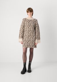 Vestido de malha bege com manchas de leopardo castanhas, mangas largas e gola canelada. Combinado com botas de tornozelo de plataforma pretas e meias transparentes.