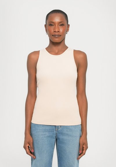 Helles beige, geripptes Tanktop mit einem Rundhalsausschnitt und ohne Ärmel. Kombiniert mit blauen Jeans, die eine enganliegende Passform und eine glatte Textur zeigen.