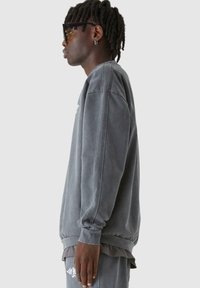 Szürke pamut pulóver ribbelt mandzsettával és szegéllyel. Lazább fazonnal és finom logó részlettel a fronton. Sima textúra, minimalista design.