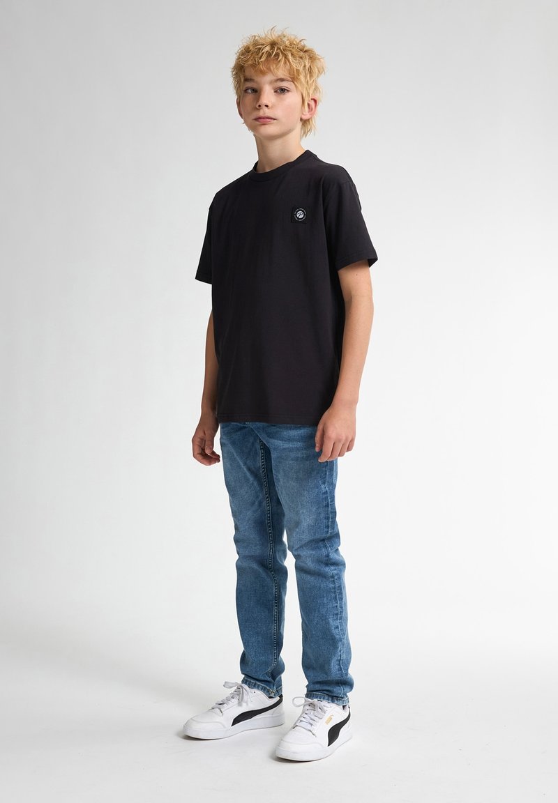 Zwarte katoen T-shirt met korte mouwen en een klein logo-opdruk op de borst, gecombineerd met lichtblauwe denim jeans en witte sneakers.