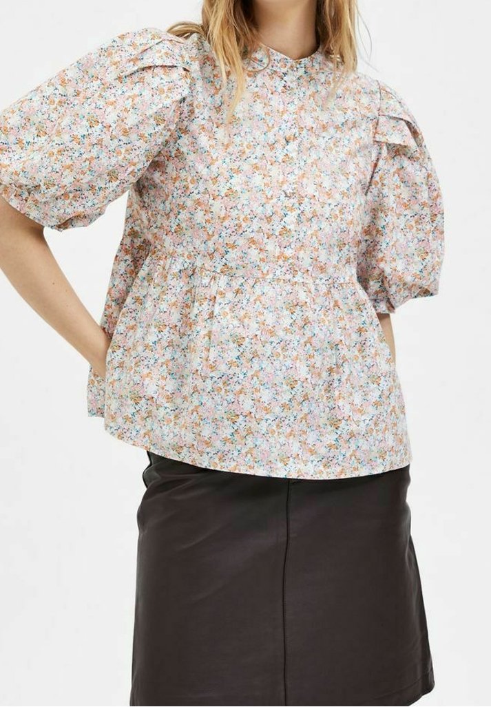 Blusa floreale con maniche corte a sbuffo, tessuto leggero, colletto rotondo e vita arricciata. Presenta una stampa floreale multicolore su uno sfondo chiaro.