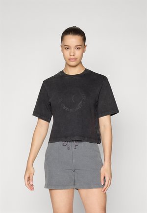 Tricou negru scurt cu o textură estompată și un logo circular în centru, combinat cu pantaloni scurți gri cu dungi și detaliu de sfoară.