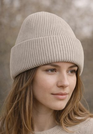 Young woman with long hair wearing a beige ribbed beanie and matching sweater, looking slightly to the right in soft natural light.