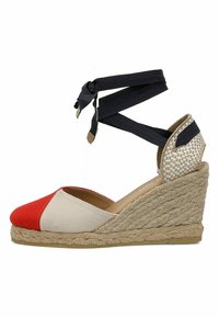 Espadrille à talon compensé en rouge, toile beige. Caractérisée par une semelle en corde de jute et des lanières à la cheville en tissu noir. Accents texturés au talon.