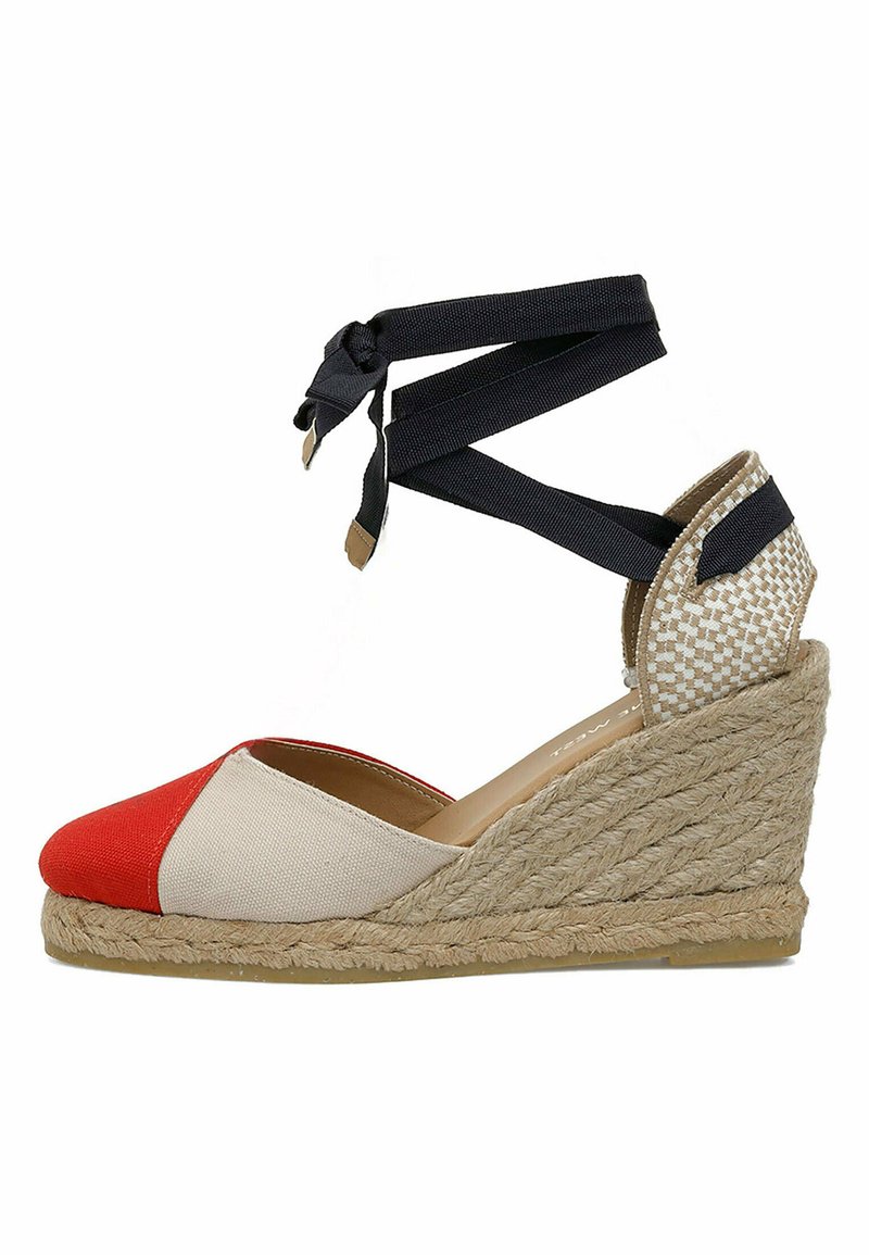 Espadrille à talon compensé en rouge, toile beige. Caractérisée par une semelle en corde de jute et des lanières à la cheville en tissu noir. Accents texturés au talon.