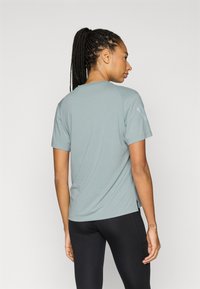 Jasnoszary sportowy T-shirt z krótkimi rękawami i luźnym krojem, z subtelnym połyskiem i logo na ramieniu.