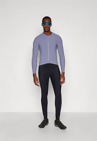 Sportovní outfit sestávající z lehce fialového přiléhavého vrchního dílu na zip a černých legín, doplněný černými sportovními botami a modře tónovanými slunečními brýlemi.