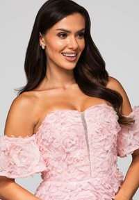 Robe rose avec texture florale, manches dénudées, et une fermeture éclair centrale. Tissu lisse avec des embellissements en rose superposés.