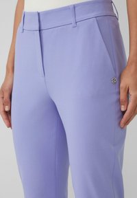 Lilafarbene Hosen aus glattem Stoff mit einem maßgeschneiderten Schnitt, vorderen Falten und einem silbernen Logo-Akzent an der Seite.