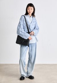 Gaiši zilā adīta džemma ar tekstūru, pārklāta pār gaiši zilo krekls. Melna ādas plecu soma ar izteiksmīgu sprādzi. Gaiši džinsa bikses.