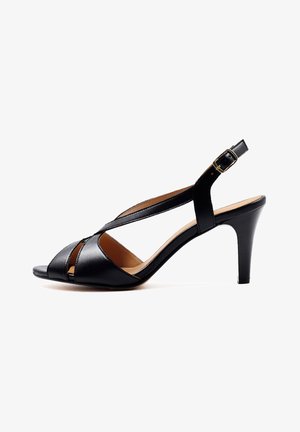 Zapato de tacón abierto con tiras en el talón de cuero negro, tacón cónico de altura media y correa con hebilla, mostrado de perfil sobre fondo blanco.