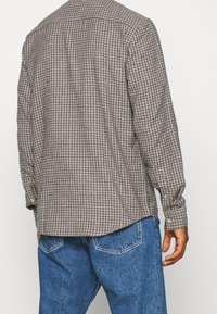 Langarmshirt in een bruin- en crèmekleurig ruitpatroon, gemaakt van geweven stof. Bevat een standaard kraag en knopenmanchetten. In combinatie met blauwe denim jeans.