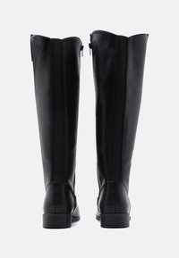 Botas de cuero negro hasta la rodilla con una textura suave, dos cremalleras laterales y un tacón bajo apilado. Paneles elásticos verticales para un ajuste ceñido.