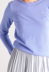 Jasnoniebieski, teksturowany sweter z okrągłym dekoltem i długimi rękawami, w połączeniu z plisowaną srebrną spódnicą. Dyskretny logo na swetrze.