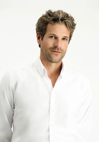 Biała koszula zapinana na guziki z kołnierzykiem, charakteryzująca się gładką fakturą. Model ma krótkie, falujące włosy i neutralny wyraz twarzy. Prosty design.