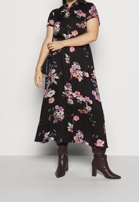 Musta kukkamekko, jossa on lyhyet hihat, napillinen etu ja lennokas malli, koristeltu eri värikkäillä kukkakuvioilla. Yhdistetty polvenmittaisiin ruskeisiin saappaisiin.