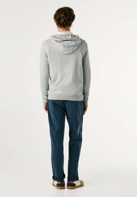 Felpa grigia con tasca a marsupio, tessuto strutturato e polsini a costine; abbinata a pantaloni blu scuro a gamba dritta e scarpe multicolori.