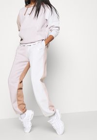 Nike sweatpants and hoodie in light pink and white, featuring color-blocked designs and a logo; paired with white sneakers.