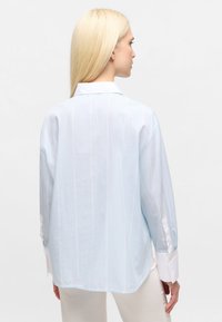 Hellblau gestreiftes Button-Up-Shirt mit langen Ärmeln, weißen Manschetten und lässiger Passform. Die Rückansicht zeigt die glatte Textur und den weichen Stoff.