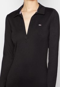 Svart långärmad polo med V-hals, med en randig krage och en liten logotyp på bröstet. Slät tyg med en åtsittande design.