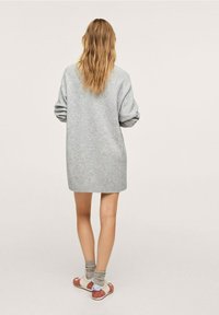 Robe-pull grise en maille avec une coupe décontractée, longueur mi-cuisse, épaules tombantes et poignets côtelés, associée à des chaussures blanches et des chaussettes grises.