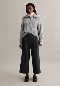 Pull gris à côtes avec un col zippé, associé à un pantalon noir large taille haute et des chaussures noires chunky. Texture lisse et coupe décontractée.