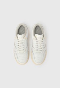 Egy pár fehér bőrből készült sportcipő bézs díszítéssel, megkötött fűzőkkel, felülnézetből, fehér háttéren.