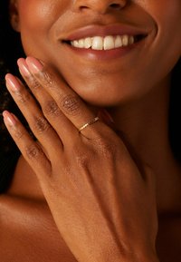 Goldring mit strukturiertem Muster, getragen an einer Hand mit natürlichem Hautton. Die Nägel sind in einem sanften Rosaton manikürt.