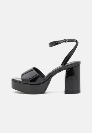 Sandales à plateforme en patent noir avec un bout ouvert arrondi, une sangle de cheville réglable et un talon épais. Surface lisse et brillante avec un décor minimal.
