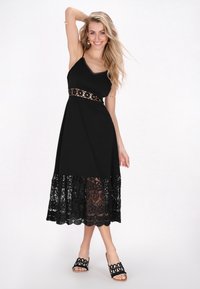 Rochie neagră cu bretele ajustabile, dantelă la tiv, detaliu cu dantelă florală la talie și siluetă A-line vaporoasă. Asortată cu sandale negre.