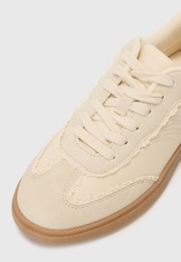 Beige sneakers with a mix of smooth and textured suede. Features round laces, stitched details, and a rubber outsole.