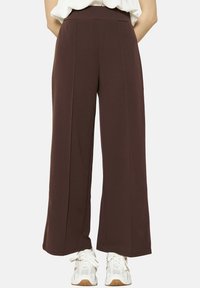 Brown wide-leg pants made of smooth fabric with a high waistband and central pleats, paired with white sneakers.