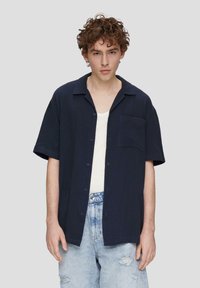 Marineblauwe short-sleeve shirt met een knoopsluiting, een enkele zak, textuurstof en een relaxed fit, gecombineerd met licht verstoorde jeans.