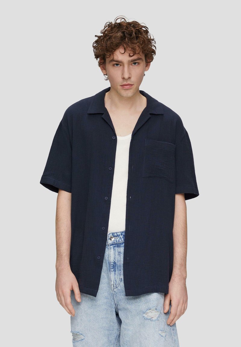 Marineblauwe short-sleeve shirt met een knoopsluiting, een enkele zak, textuurstof en een relaxed fit, gecombineerd met licht verstoorde jeans.