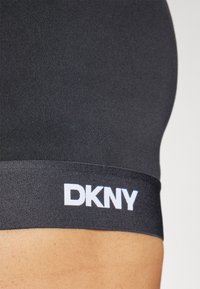 Faixa de tecido elástico preto com o logo branco "DKNY". Textura suave, design ajustado, adequada para roupa de desporto ou roupa de casa.