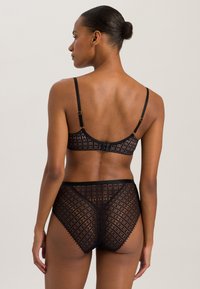 Musta pitsinen rintaliivipari ja korkeavyötäröiset alushousut esittelevät geometrisia kuvioita, joissa on läpinäkyviä osia. Olkaimet ovat säädettävät ja niissä on kultaiset yksityiskohdat.